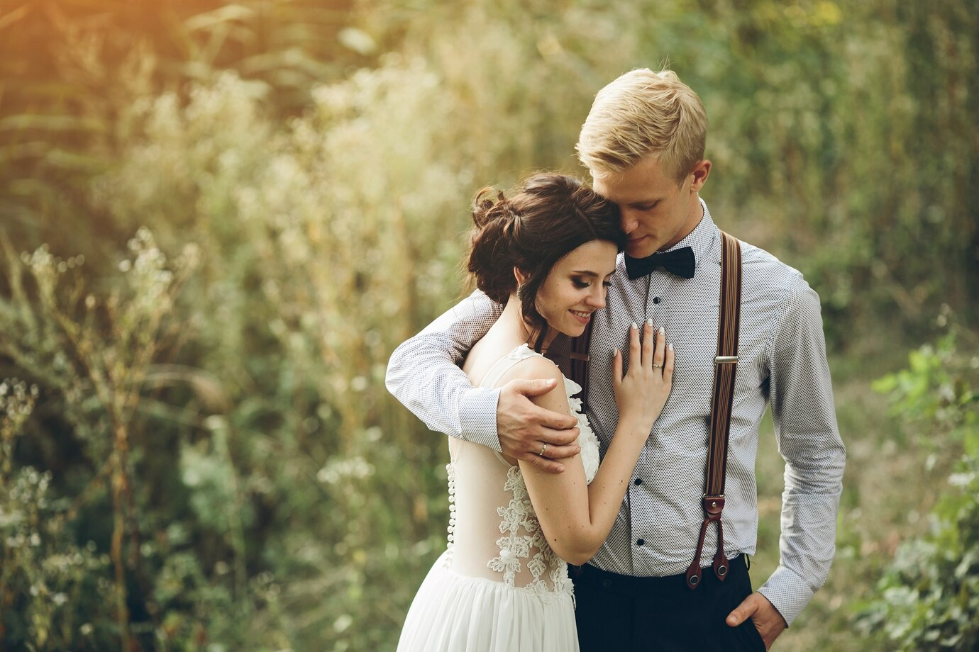 well-dressed young man with his right arm around the shoulder of a young woman wearing a wedding dress outdoors well-dressed young man with his right arm around the shoulder of a young woman wearing a wedding dress outdoors