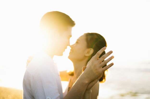 man and woman standing close fact to face bright sun in background