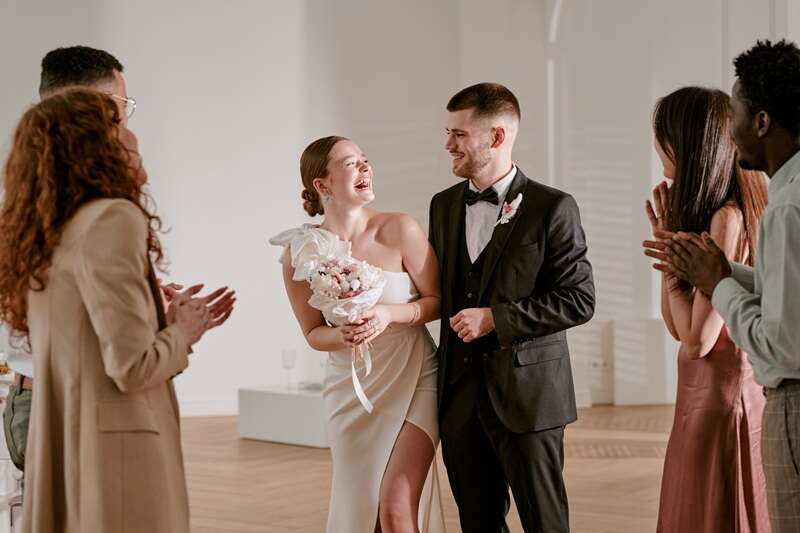 Caucasian Young Adult Bride Laughing with Groom Surrounded by Diverse Friends